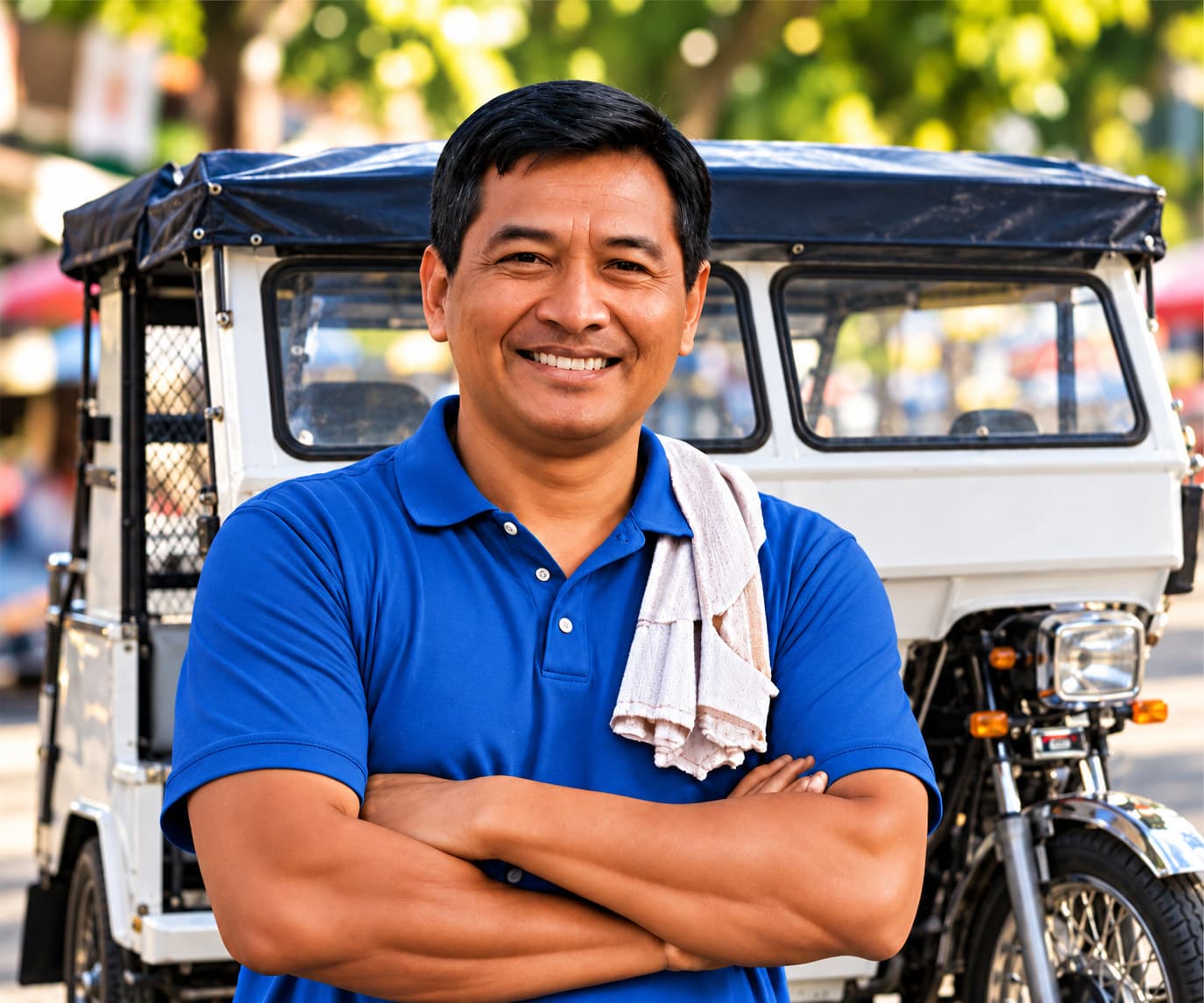 A smiling tricycle driver in a blue polo, a towel over his shoulder, stands with his arms crossed in front of his white tricycle.